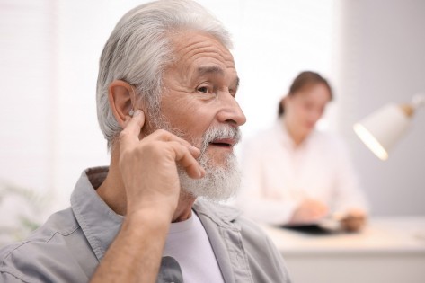 Senior man with hearing aid and doctor working in hospital, selective focus