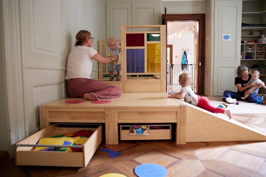 Ein Kind krabbelt den Holzspielplatz hinauf, während ein anderes zuschaut.