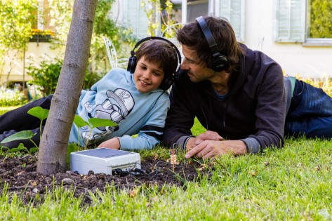 Zwei Personen liegen auf einer Wiese und tragen Kopfhörer. Sie lauschen den Geräuschen im Boden unter ihnen.