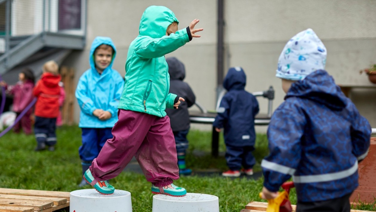 Kinder spielen im Garten. Ein Kind balanciert über Eimer.