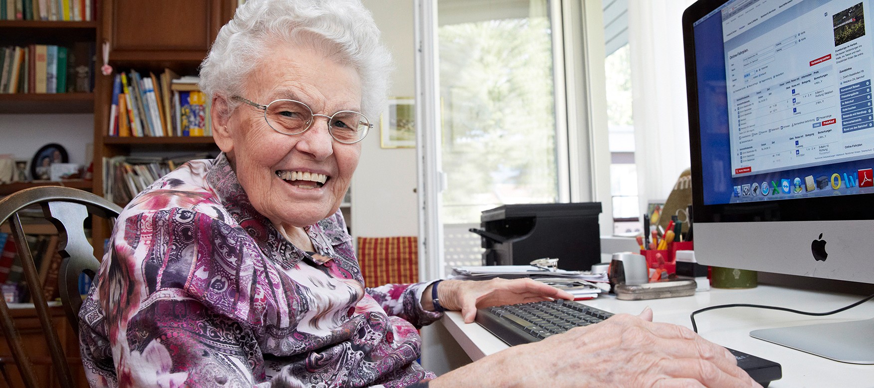 Eine Seniorin sitzt lachend am Computer.