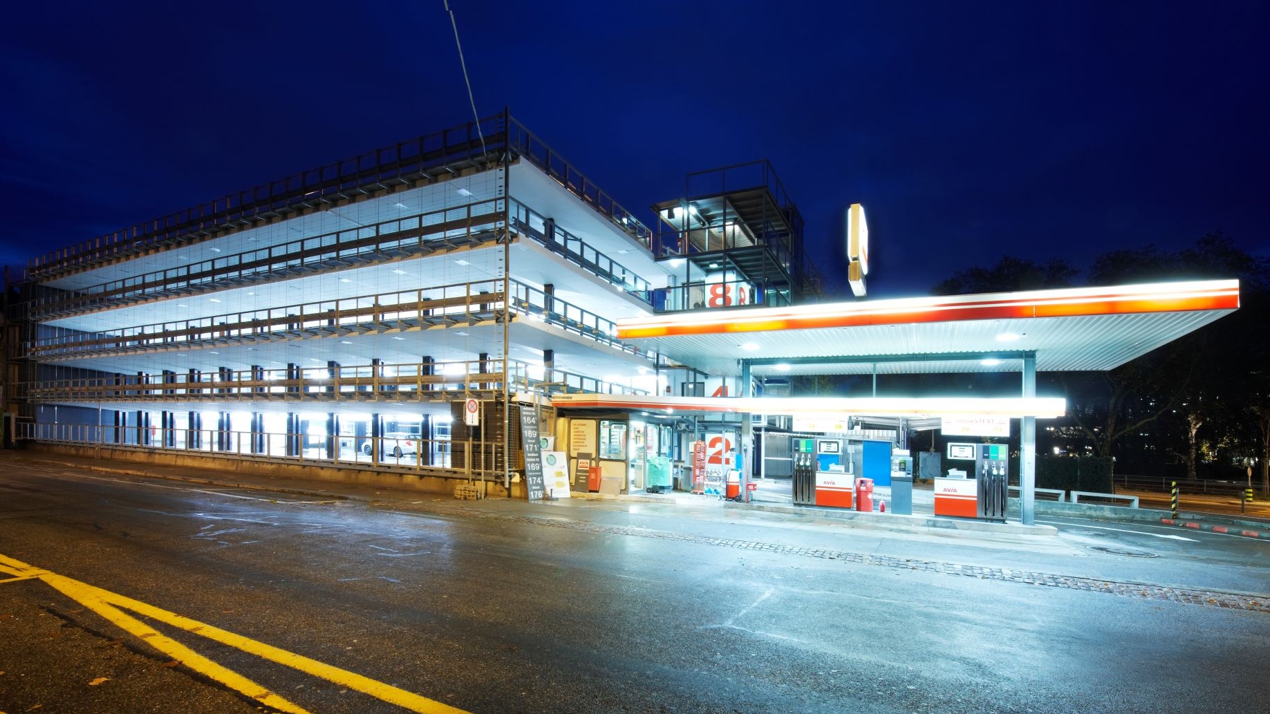 Parrkhaus neben geld-orange beleuchteter Tankstelle in der Nacht.