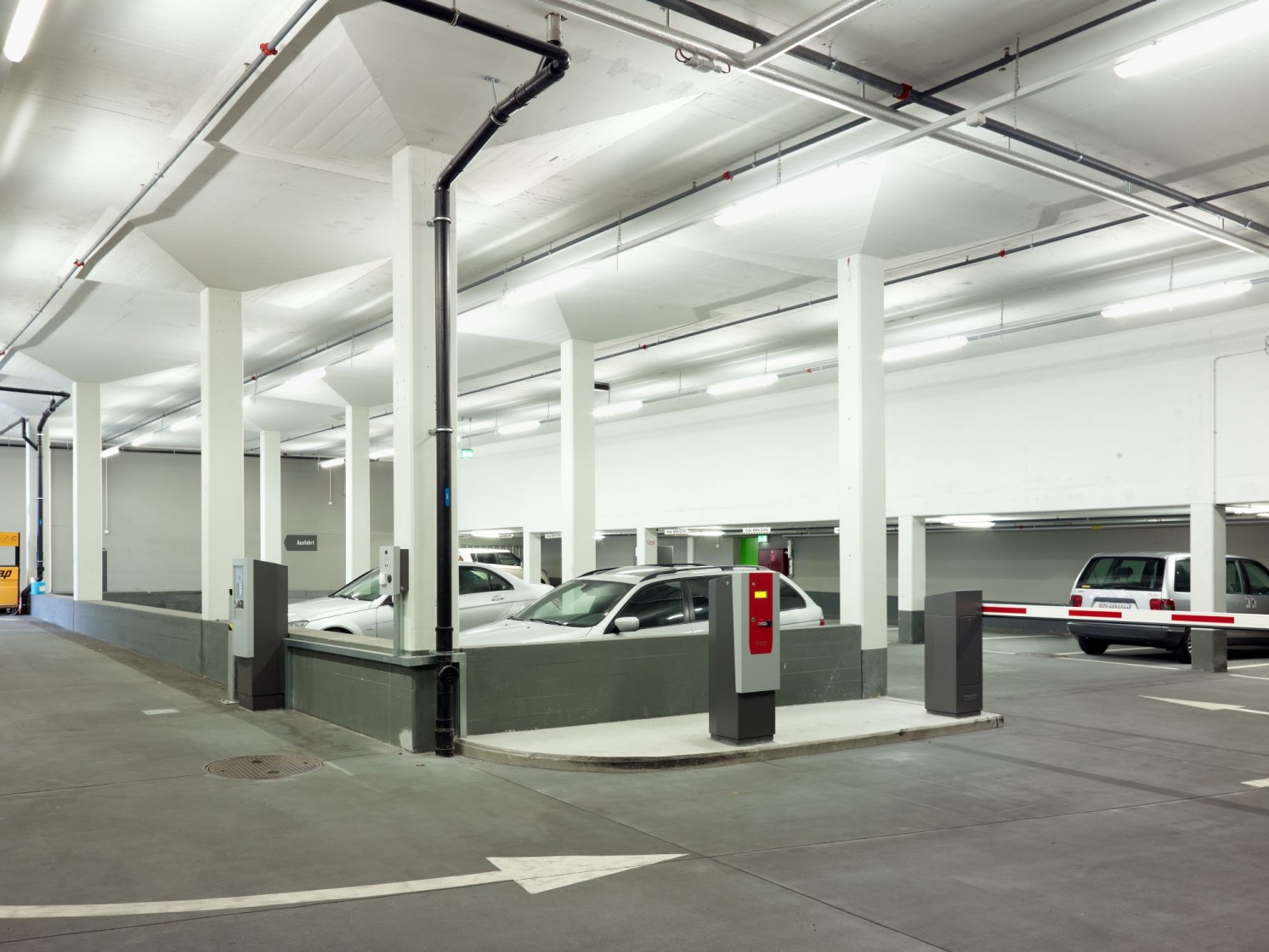 Weisse Autos, in einem Parkhaus mit dunklem Boden und einer Schranke. Bild: Luca Zanier
