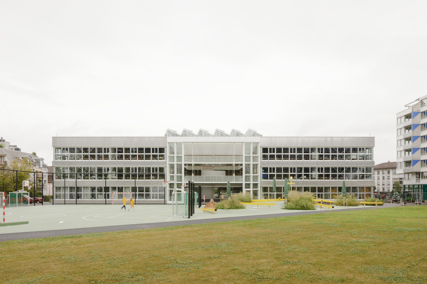Das Foto wirft einen Blick über die grüne Wiese auf das Gebäude der neuen Schulanlage.
