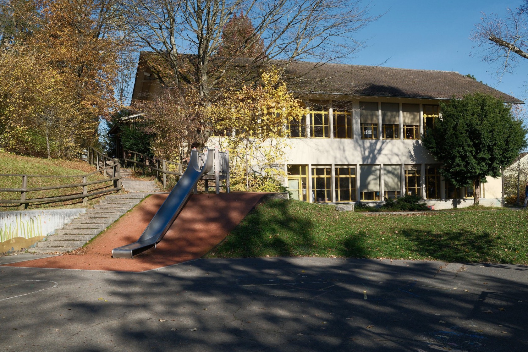 Aussenansicht des Kindergarten Bruderwies mit Grünfläche und Spielplatz im Vordergrund.