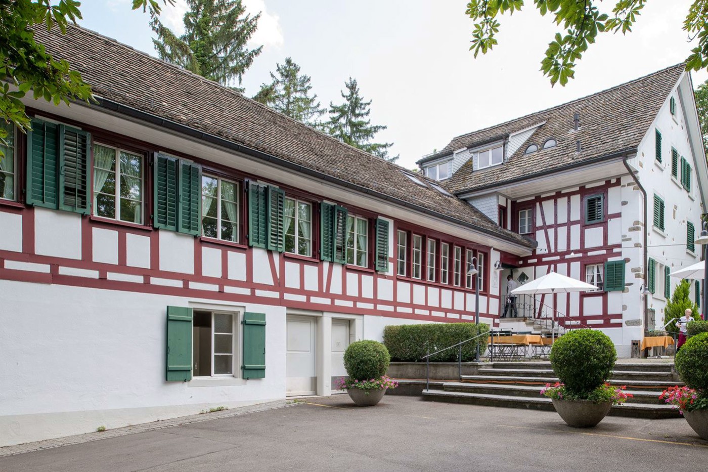 Traditionelles Restaurant Muggenbühl in einem historischen Fachwerkgebäude mit weisser Fassade und roten Holzbalken, grünen Fensterläden und Schindeldach.