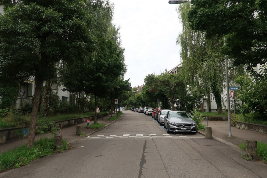 Strasse mit Parkplätzen, auf der Seite hat es Bäume