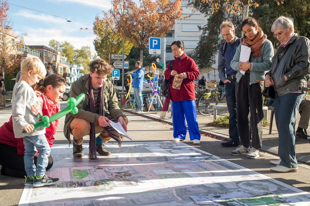 Mehrere Personen betrachten den auf der Strasse ausgebreiteten Plan des Quartiers