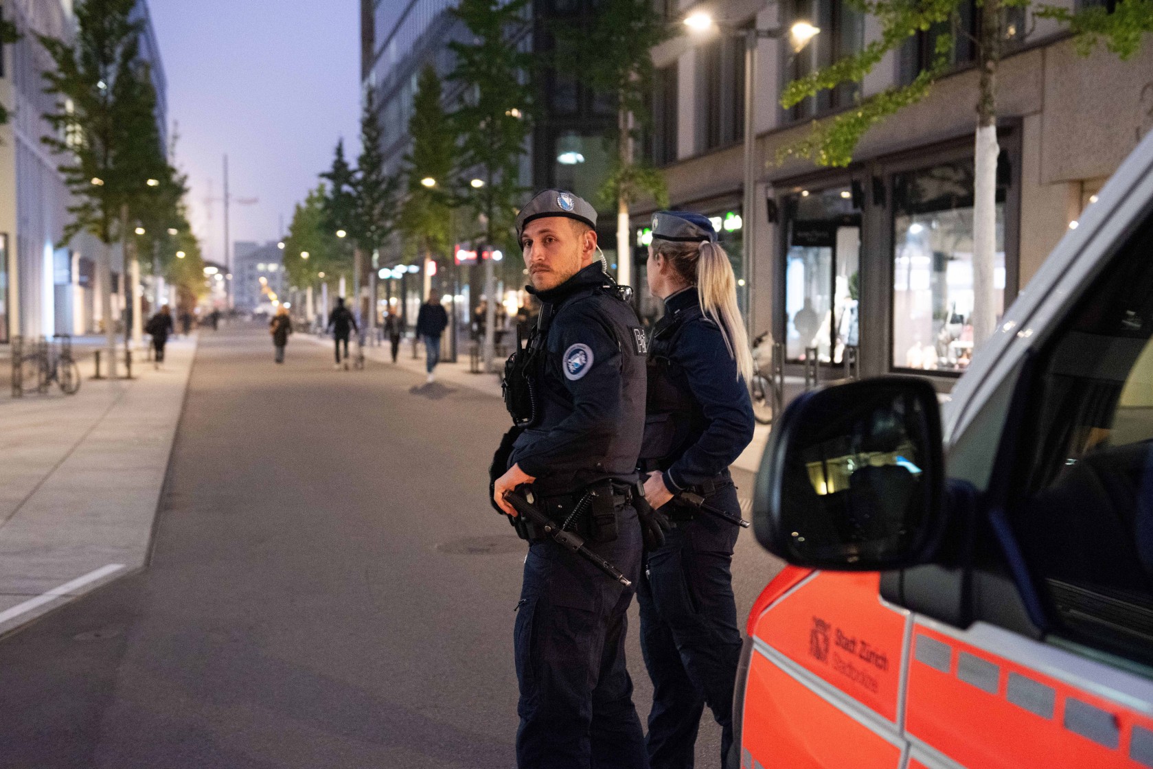Zwei Polizist*innen bei Polizeiauto am Abend.
