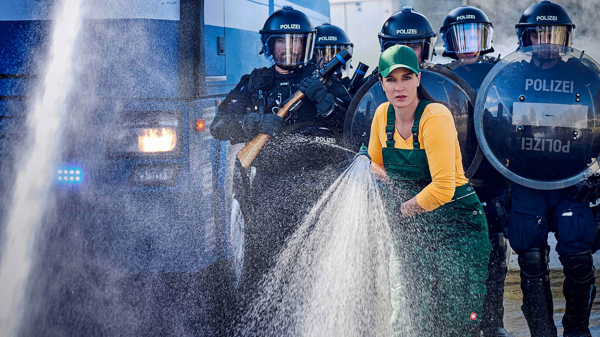 Gärtnerin mit Schlauch und im Hintergrund Polizist*innen in Uniform.