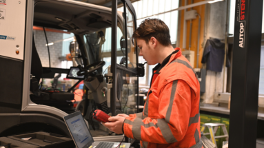Motorgerätemechaniker in oranger Areitskleidung bei der Arbeit an einem Nutzfahrzeug