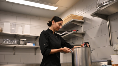 Küchenangestellte in schwarzer Kleidung beim Hantieren mit einem Kochtopf in einer Küche