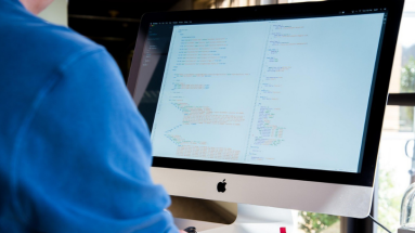 Person in blauem Pulli vor Bildschirm