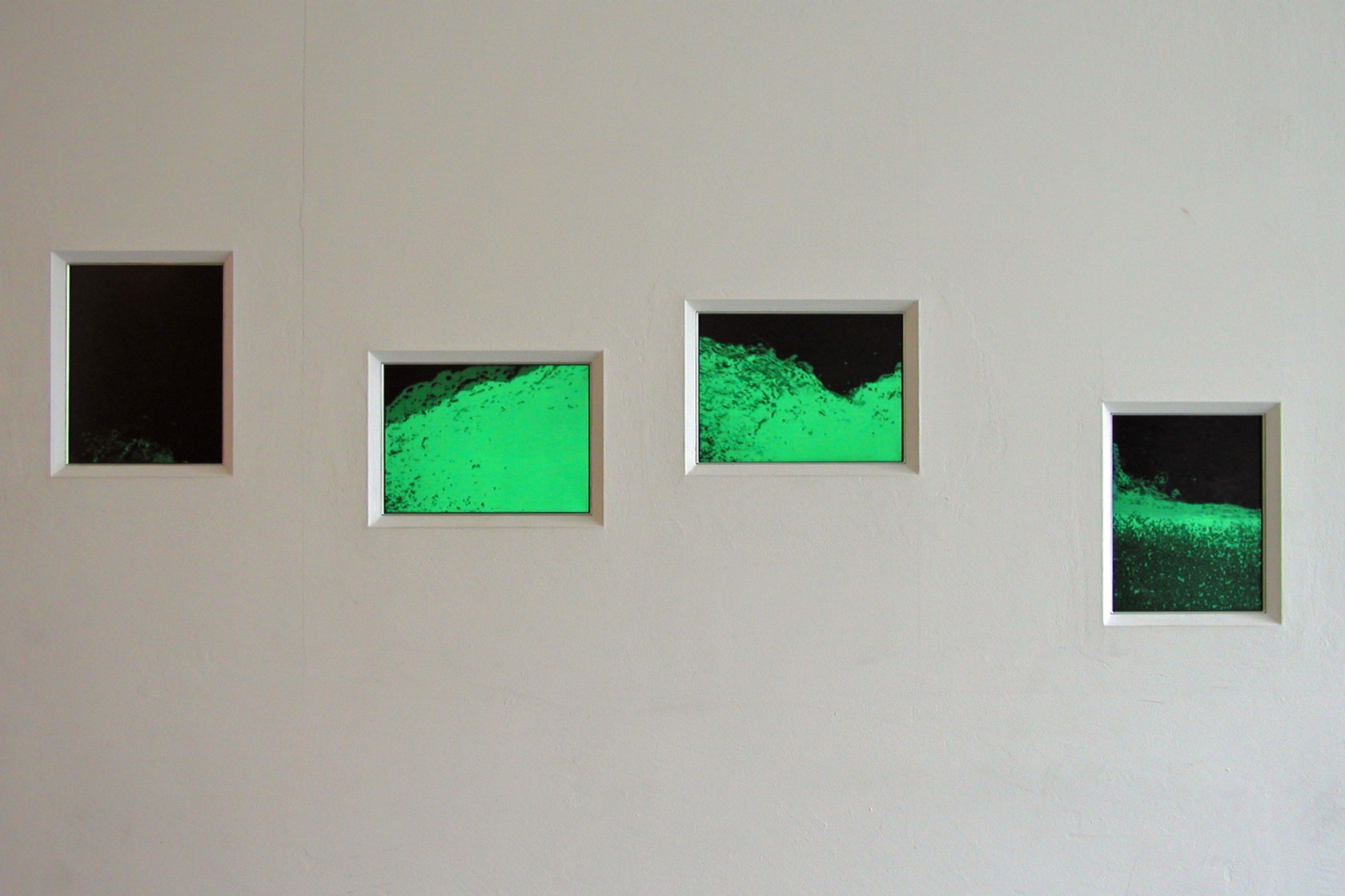eine Reihe von vier hoch- und querformatigen, rechteckigen Fenstern in einer Wand eingelassen, mit schwarz grünen, abstrakten Bildern