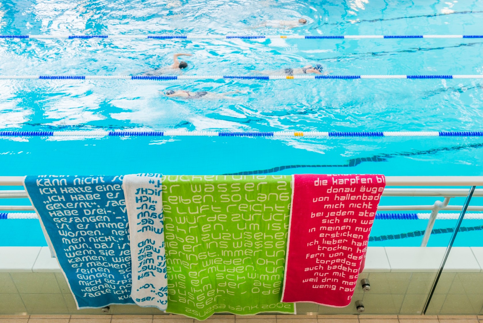 Farbige Badetücher hängen auf einem Geländer beim Schwimmbecken