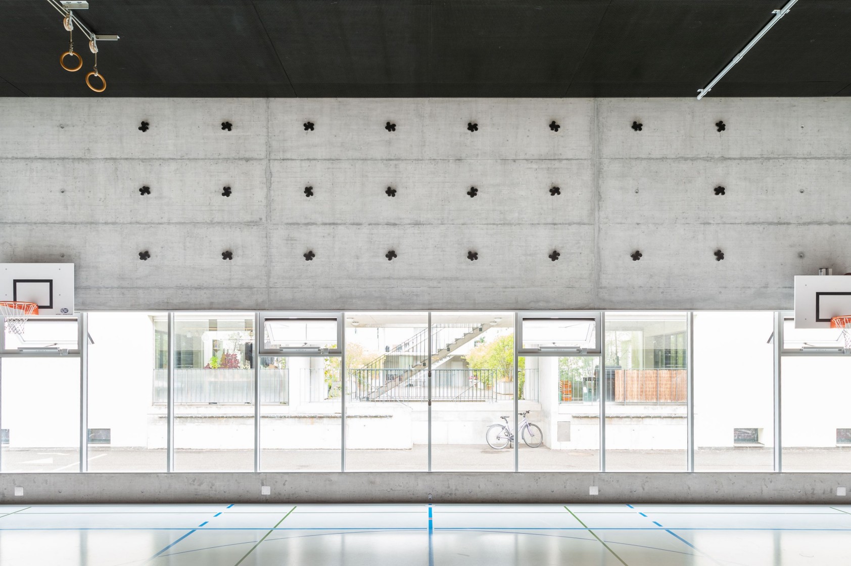 Sporthalle mit auf Betonwand platzierten Stahlfiguren, Sicht durch Fensterfassade auf Strasse