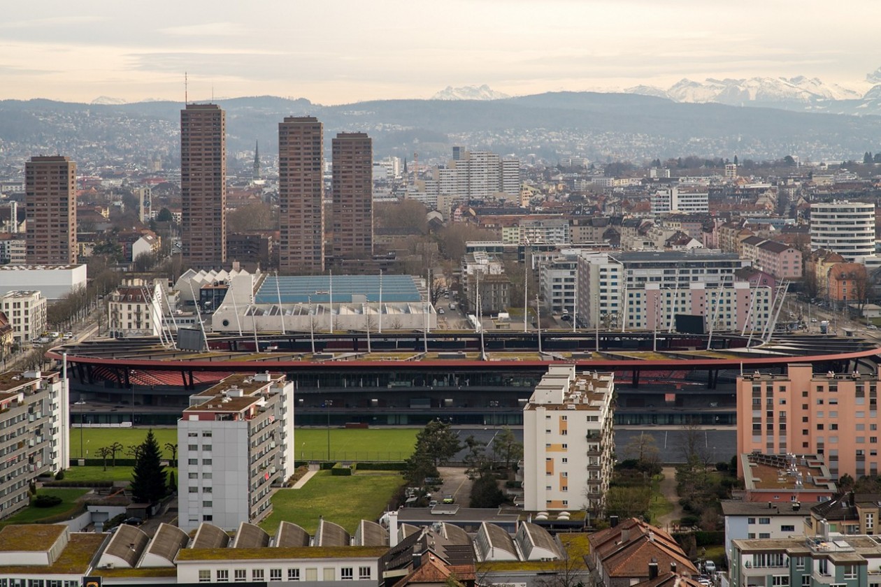 blick über stadt mit Stadion, Hochhäusern und Berge im Hintergrund
