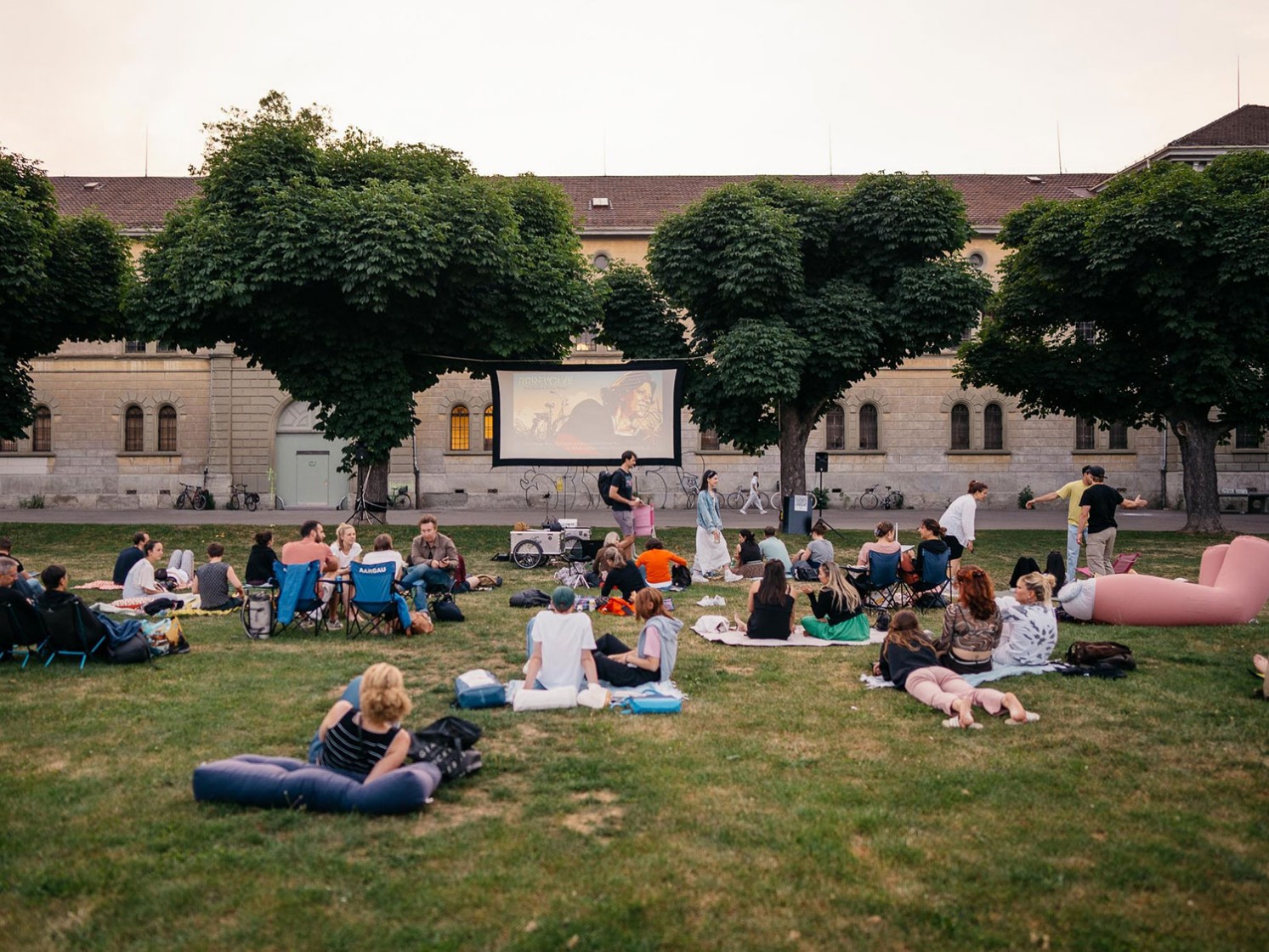 Foto von Personen, die auf der Kasernenwiese sitzen und einen Filmvorführung des Projekts Cinema Solaire schauen.