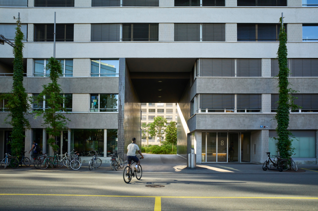 Mann auf Velo vor Wohngebäude mit Hofeinfahrt.